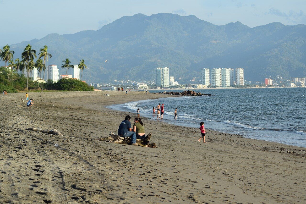 People sitting on sand, white buildings in background