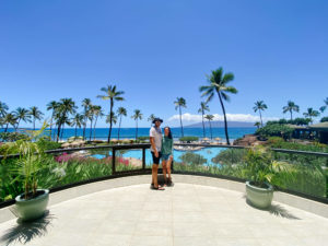 man and woman standing in front of blue water and palm trees