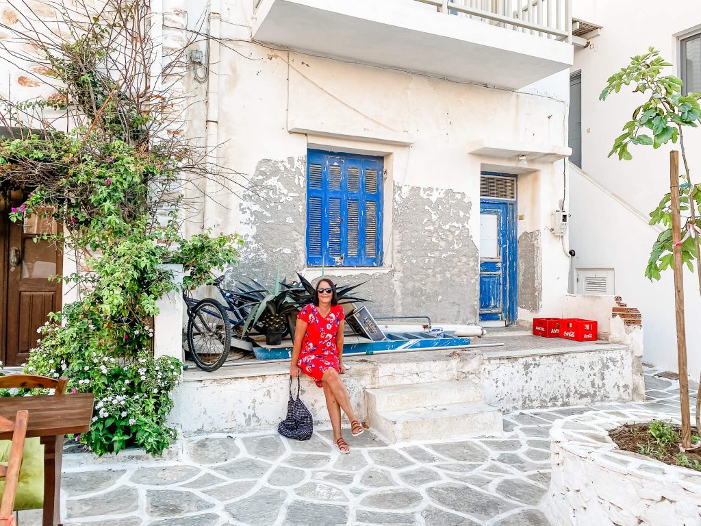 woman in red dress sitting in front of white building with blue shutters