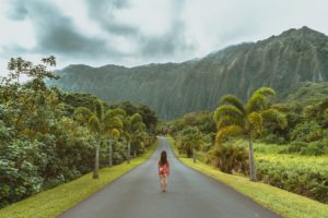 Girl walking down road with palm trees on side of road