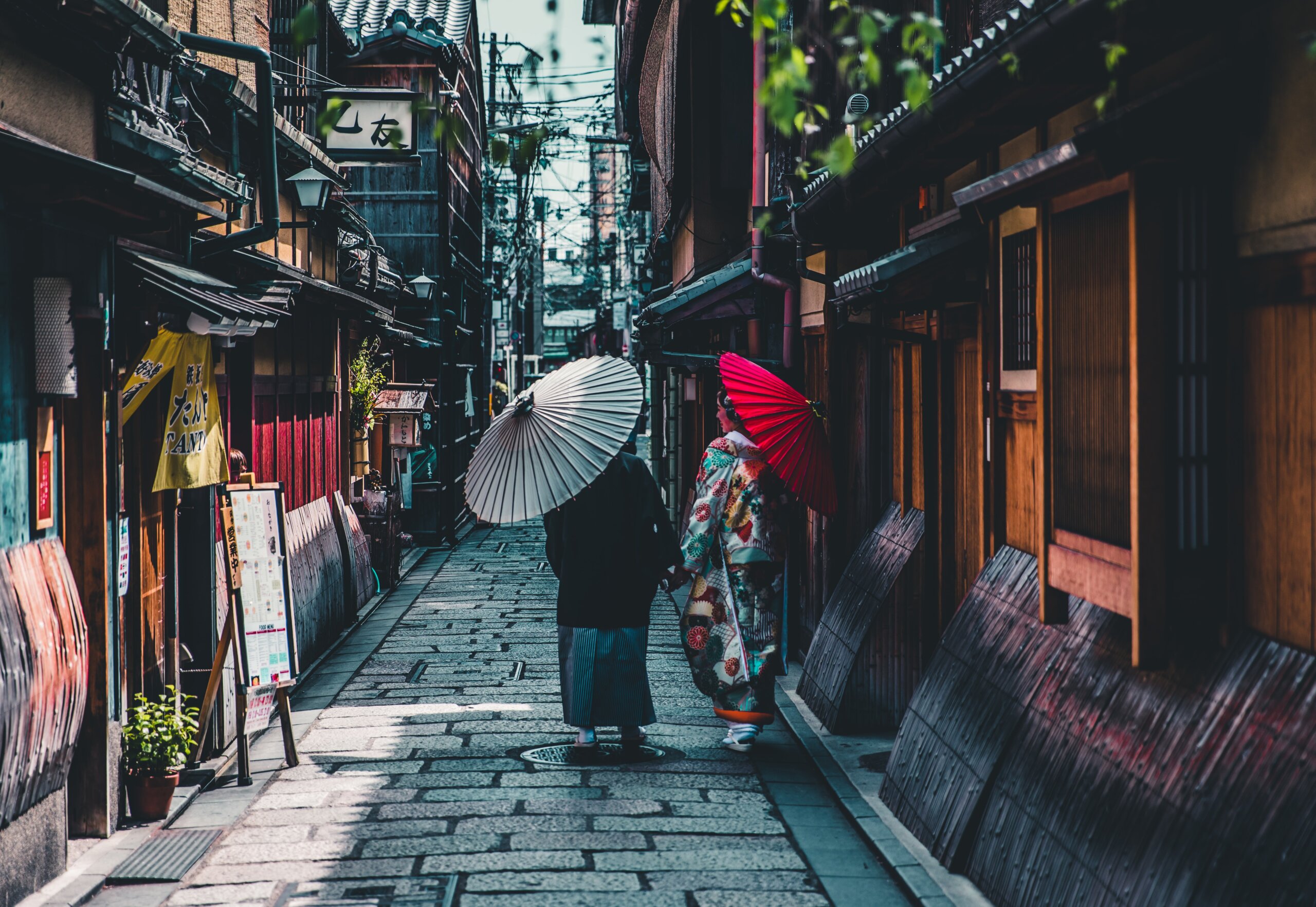 Women with parasols wearing kimonos walking down a street