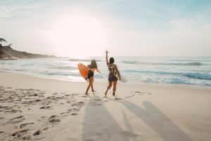 Two girls walking on beach with surfboards