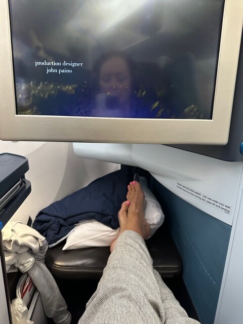 Feet on footwell under tv on airplane.