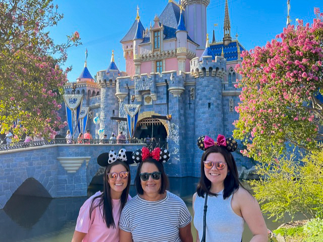 Three women with mouse ears standing outside castle