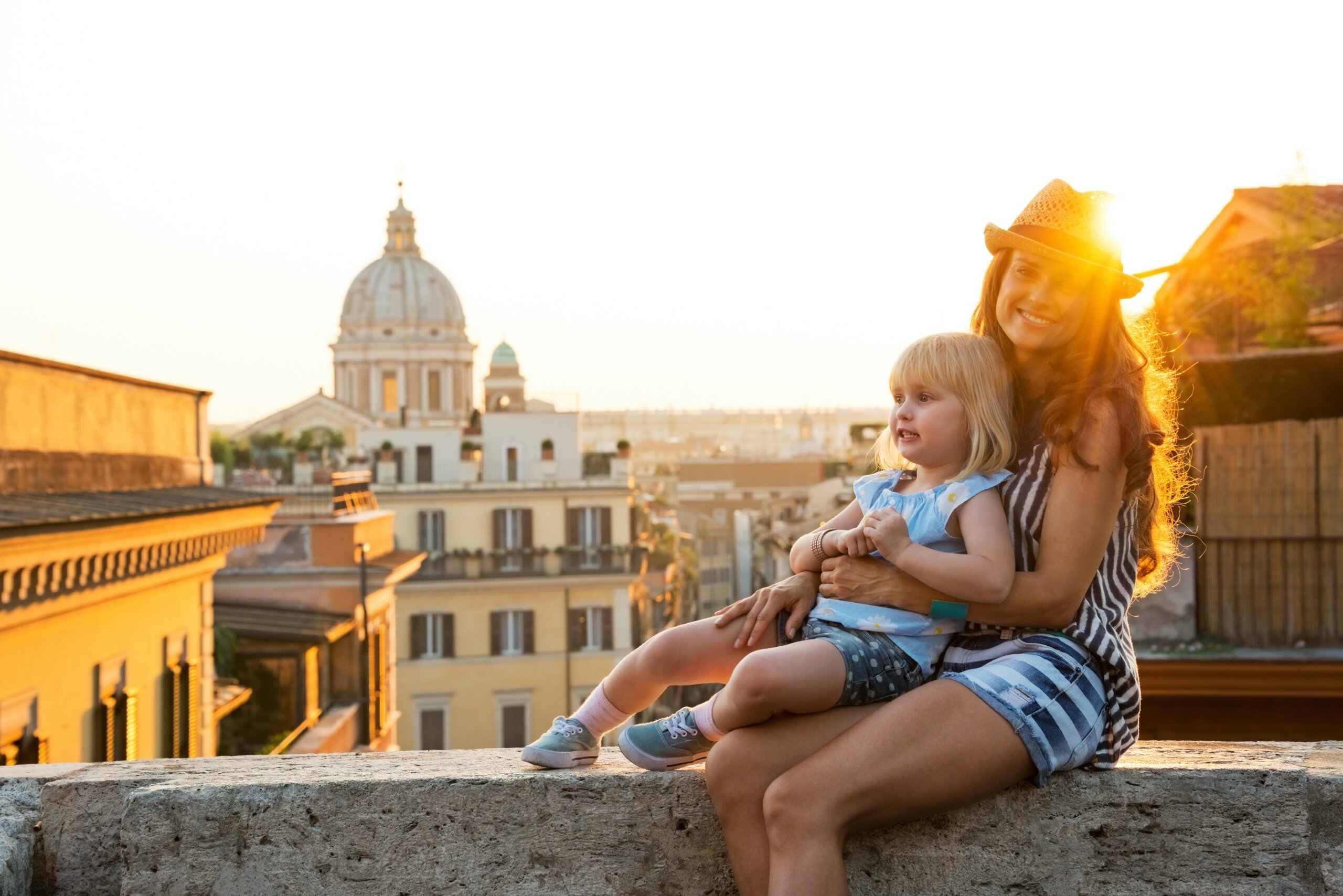 Woman and young girl sitting on wall overlooking city