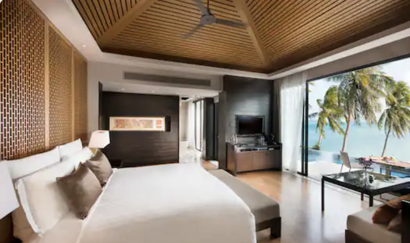 Hotel bedroom with view of ocean and palm trees.